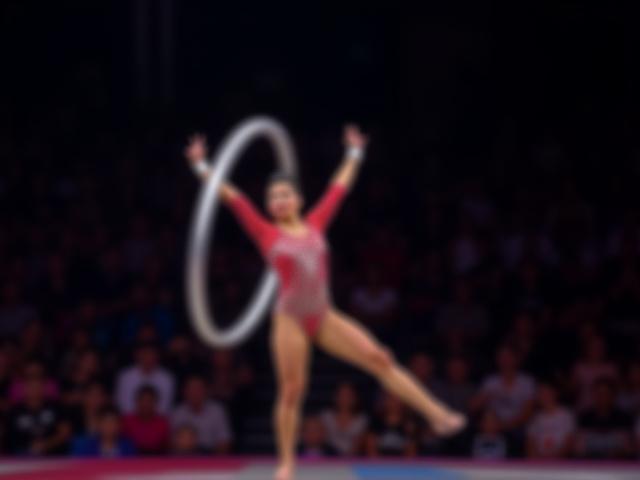 Gimnasta rítmica realizando una pose artística con un aro en una competencia. Vista frontal.